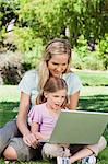 A mom and her daughter surfing the internet together on a laptop in the park