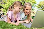 A smiling mom and child surfing the web together on a laptop in the park