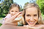 A smiling girl resting upon her mother's shoulder in the park