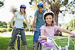 A smiling family on their bikes wearing helmets in the park