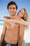 Young happy couple embracing and smiling while sunbathing on the beach