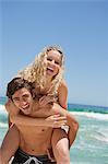Jeune homme souriant, donnant sa petite amie un piggy-back en se tenant debout en face de la mer