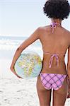 Rear view of a young woman standing in front of the ocean with a globe beach ball