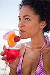 Young attractive woman sipping a strawberry cocktail while sitting on the beach