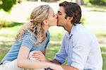 Side view of a young couple sitting and kissing on the lawn