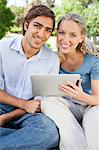 Sourire de jeune couple assis dans le parc avec son ordinateur tablette
