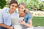 Sourire de jeune couple avec une tablette PC assis dans le parc