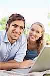 Smiling young couple lying on the lawn with their laptop