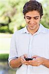 Smiling young man reading a text message in the park