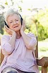 Woman listening to music with her eyes closed and her hands holding headphones to her ears as she sits on a bench