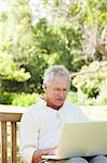 Man Blick auf etwas auf einem Laptop sitzen auf einer Holzbank in einem park