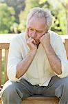 Disappointed man resting his face in his hands as he sits on a bench in a park