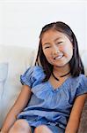 A young smiling girl sitting on the couch and looking straight ahead.