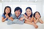 A smiling family sit together in the room with a window