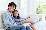 A dad and his daughter smiling for the camera as they sit on the couch together