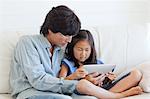 A daughter gets help from her dad on how to use the tablet while sitting on the couch