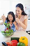 A close up shot of a mother and daughter tossing a salad together