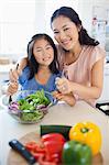 A smiling mother and daughter look ahead as they toss a salad together