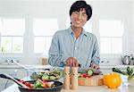 A smiling man looks forward as he prepares a salad in the kitchen