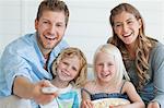 A laughing family watch tv as the dad changes the channel and the daughter holds a bowl of popcorn
