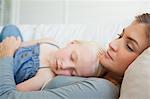 A mother with her daughter asleep on her chest as they sleep on the couch