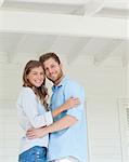 A woman and man looking straight ahead and embracing while smiling