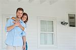 A smiling wife holding onto her husband as they stand on the porch while looking forward