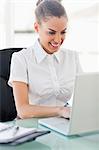 Frizzy haired smiling woman working on a laptop in a bright office