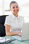 Portrait of a frizzy haired smiling woman working on a laptop in a bright office
