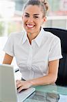 Portrait of a beaming frizzy haired woman working on a laptop in a bright office