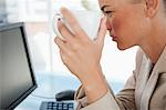 Close-up of a woman holding a mug on a glass desk while looking at her screen