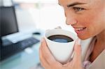 Close-up of a businesswoman with a coffee in front of her computer