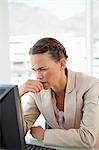 Businesswoman with braids frowning in front of her screen in a bright office