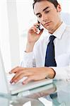 Businessman using a smartphone while typing his laptop in a bright office