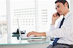 Businessman calling while tapping his laptop in a bright office