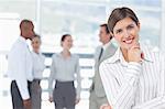 Thoughtful smiling young saleswoman with colleagues behind her