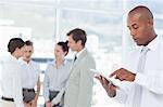 Young salesman using tablet computer with colleagues behind him