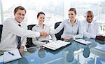 Smiling young businesspeople shaking hands while sitting at a table