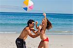 Junges Paar in spielen mit einem Beach Ball am Strand schwimmen-Anzug