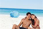 Cute couple sitting on the beach with a parasol and the sea in background