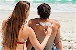 Rear view of a woman applying sunscreen on her boyfriend while sitting in front of the sea
