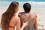 Rear view of a woman applying sunscreen in form of heart on her boyfriend while sitting in front of the sea