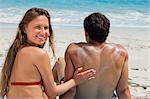 Rear view of a woman applying a heart of sunscreen on her boyfriend while sitting in front of the sea