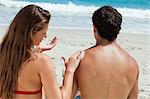 Rear view of a woman applying sunscreen on the shoulder of her boyfriend in front of the sea