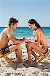 Lovers face to face in folding chair with the sea in background