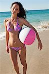 Portrait einer Frau im Bikini ein Strandball mit dem Meer im Hintergrund halten