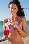 Femme en mélangeant un cocktail avec une paille tout en portant un bikini comme elle se trouve sur une plage