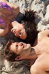 Couple allongé sur une plage de sable souriant tout en portant des maillots de bain