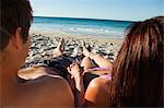 Rear view of a couple lying on the sand while holding hands in front of the sea