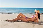 Portrait of a gorgeous woman lying on the sand while wearing a hat